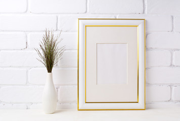 Gold decorated frame mockup with dark grass in vase near brick wall