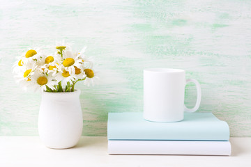 White coffee mug mockup with white field chamomile bouquet in handmade rustic vase and books