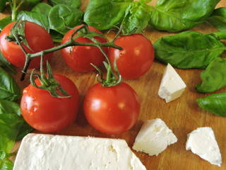 Cherry tomatoes, basil, cheese on a wooden board