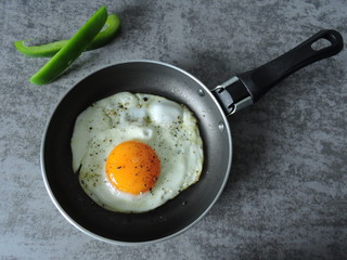 Fried egg on a frying pan, pieces of bell pepper on a gray background. Top view