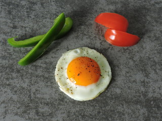 Fried egg with black pepper, tomato slices and bell pepper on a gray background. Close up, top view.