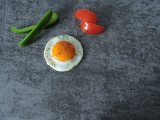 Fried egg with black pepper, tomato slices and bell pepper on a gray background. Top view.