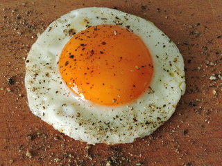 Fried egg with black pepper on a wooden surface.Close up