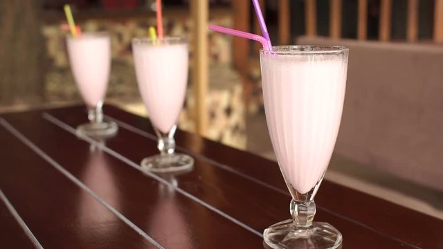 Three fruit milkshakes on a wooden table in an outdoor cafe. One glass in the field, two blurred.