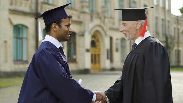 Eminent professor giving diploma to male student shaking hand convocation day