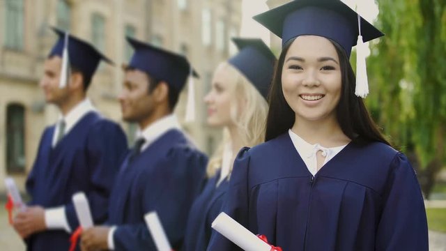 Asian graduate student with diploma, smiling into camera, international studies