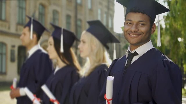 Mixed-race graduate student with diploma smiling into camera, exchange program