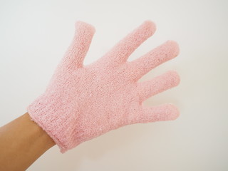 Left hand wearing pale pink scrubbing glove, on white background