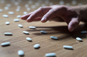 Drug addict with withdrawal symptoms reaching out to many pills on the floor with hand. Drug addiction, medical abuse and narcotics hook and dependence concept. Tablet overdose.