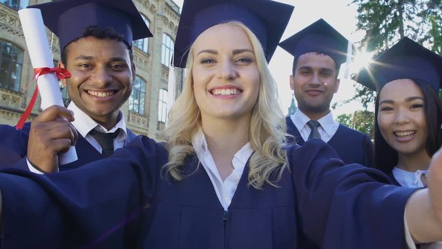 Classmates in academic regalia taking selfie on graduation day, achievement
