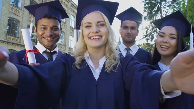 College graduates taking selfie on graduation day saying cheese, friendship