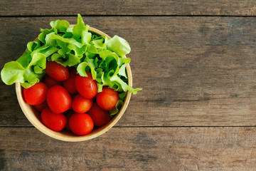 Fresh tomato and lettuce in wood bowl put on wood table. Top view or flat lay of tomato and green oak lettuce with copy space for background. Fresh green oak lettuce and tomato prepare for cooking.