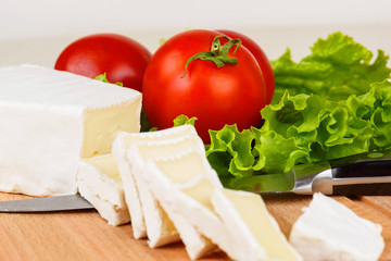 Cheese slices, tomatoes and lettuce leaf for breakfast on a wooden cutting board.