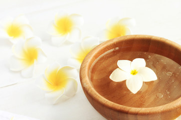 Fototapeta na wymiar White tropical flower plumeria (frangipani) in brown wooden bowl of aroma scented water, beauty spa treatment preparation. Light floral background empty space. 