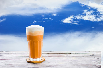 Thai tea frappe (Cha-Thai) on wood table with clouds and sky background. Conceptual tea time for...