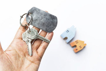 Girl hand holding hose key over blurred miniature house on white background, property and real estate concept