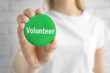 Woman holding badge with word VOLUNTEER on light background
