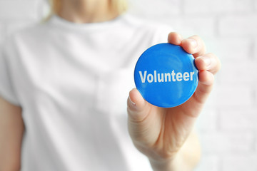 Woman holding badge with word VOLUNTEER on light background