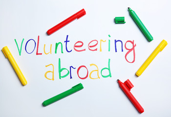 Text VOLUNTEERING ABROAD and felt-tip pens on white background