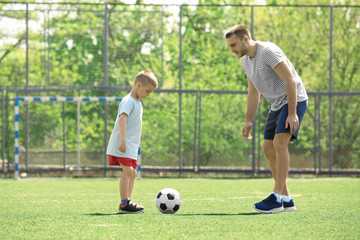 Father and son playing football on soccer pitch