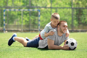 Father and son with ball lying on soccer pitch