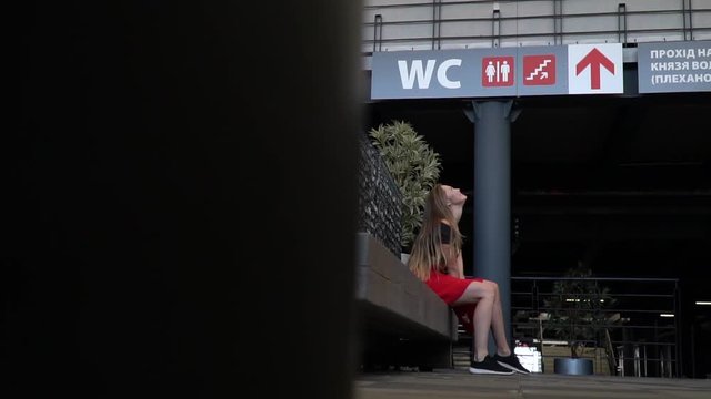 The girl is sitting on the bench and holding her breath so she does not urinate while waiting for the queue for the toilet in the mall, slow motion