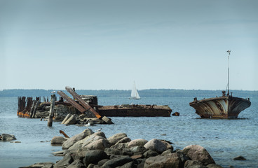 Old broken boat wreck on the shore, blue sea and sailboat on background. Harilaid, small island in Estonia, Europe.