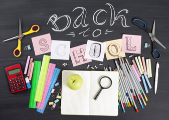 "Back to school" handwritten with school supplies on a black background. Top view.