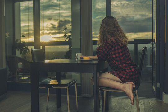 Woman having breakfast by window in city apartment