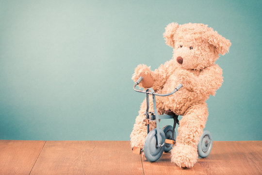 Teddy Bear is sitting on old retro toy bicycle in front mint green background. Vintage style filtered photo