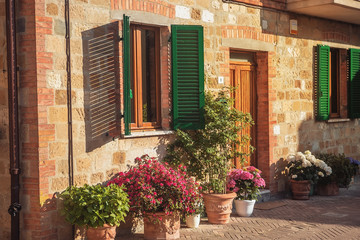 Fototapeta na wymiar Beautiful stone house with windows, green shutters and flowers. Pienza, Italy.