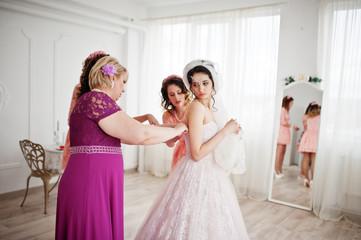Naklejka premium Helpful bridesmaids and mother helping bride to tie the dress up in big light room.
