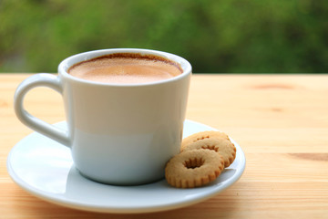 One Cup of Hot Coffee with Cookies Served on Wooden Table with Blurred Green Bush in Background 