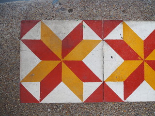 Old dirty red, yellow, and white star pattern ceramic tile floor, with grainy texture stone background