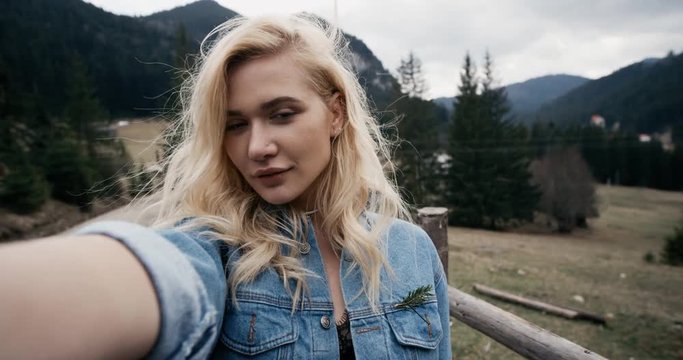 Blonde girl. Beautiful young woman taking selfie on countryside at sunset. Beauty model girl enjoying nature outdoors. Slow motion. 4k