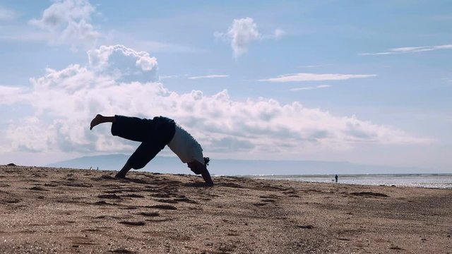 Indonesian man silhouette doing yoga poses on beach. Shot with Sony a7s and Atomos Ninja Flame in the morning with blue sky.