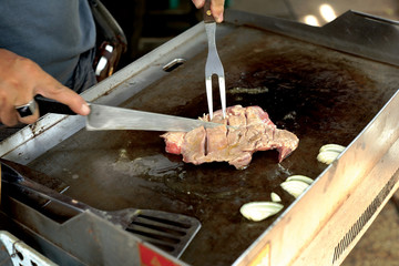 People grilling pork steak on plat pan.