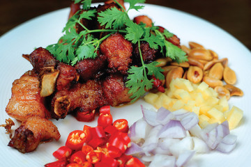 Thai style deep fried pork ribs bone served with chili, shallots, ginger, fried beans on white plate.