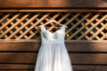 Beautiful white wedding dress hanging on hanger on the balcony of wooden house outdoors, free space