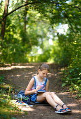 Fototapeta premium Girl painter draws in a park sitting on the ground.