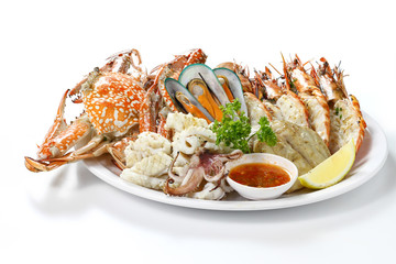 Grilled Mixed Seafood Contain Big Prawns, Mussels, Blue Crabs, Calamari Squids and Roasted Barracuda Fish Garlic with Spicy Chili Sauce and Lemon on Plate, Isolated on White Background with Shadow.