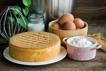 Homemade sponge cake on white plate.Soft and lite delicious sponge cake with ingredients: eggs flour milk on wood table. Homemade cake with ingredients in homemade bakery concept for bakery background