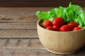 Fresh tomato and lettuce in wood bowl put on wood table. Side view close up of tomato and green oak lettuce with copy space for background. Fresh green oak lettuce and tomato prepare for cooking.