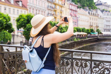 Woman taking pictures with smartphone. Stylish summer traveler woman in hat with camera outdoors in...