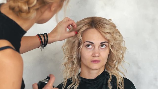 Hairdresser fixes lacquer curls in beauty salon, close up