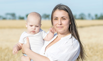Portrait of a beautiful young mother and small newborn baby in wheat field at sunny summer day