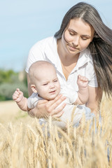 Portrait of a beautiful young mother and small newborn baby playing in wheat field at sunny summer day