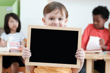 Fototapeta na wymiar Cute boy holding blank blackboard in classroom, education concept background