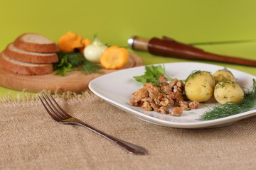 Fried chanterelles and boiled potatoes with dill are served on a white ceramic plate. Natural food from mushrooms and vegetables on a green wooden background.