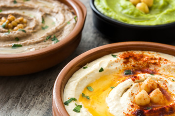Different hummus bowls. Chickpea hummus, avocado hummus and lentils hummus on wooden table
